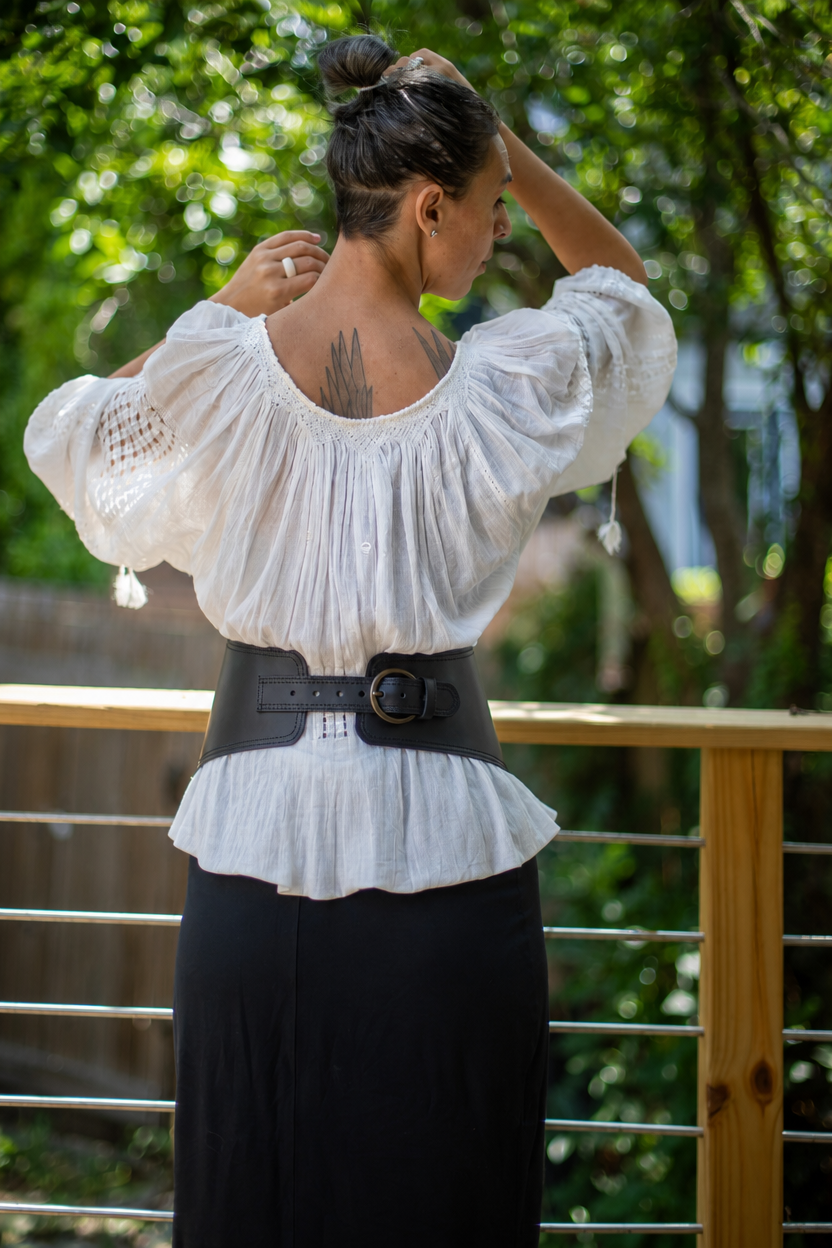 Black leather corset waist belt with brass buckle, worn over white peasant blouse