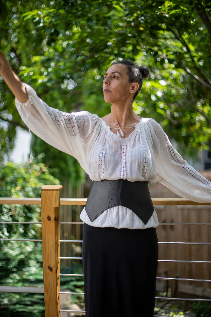 Black leather corset waist belt with brass buckle, worn over white peasant blouse