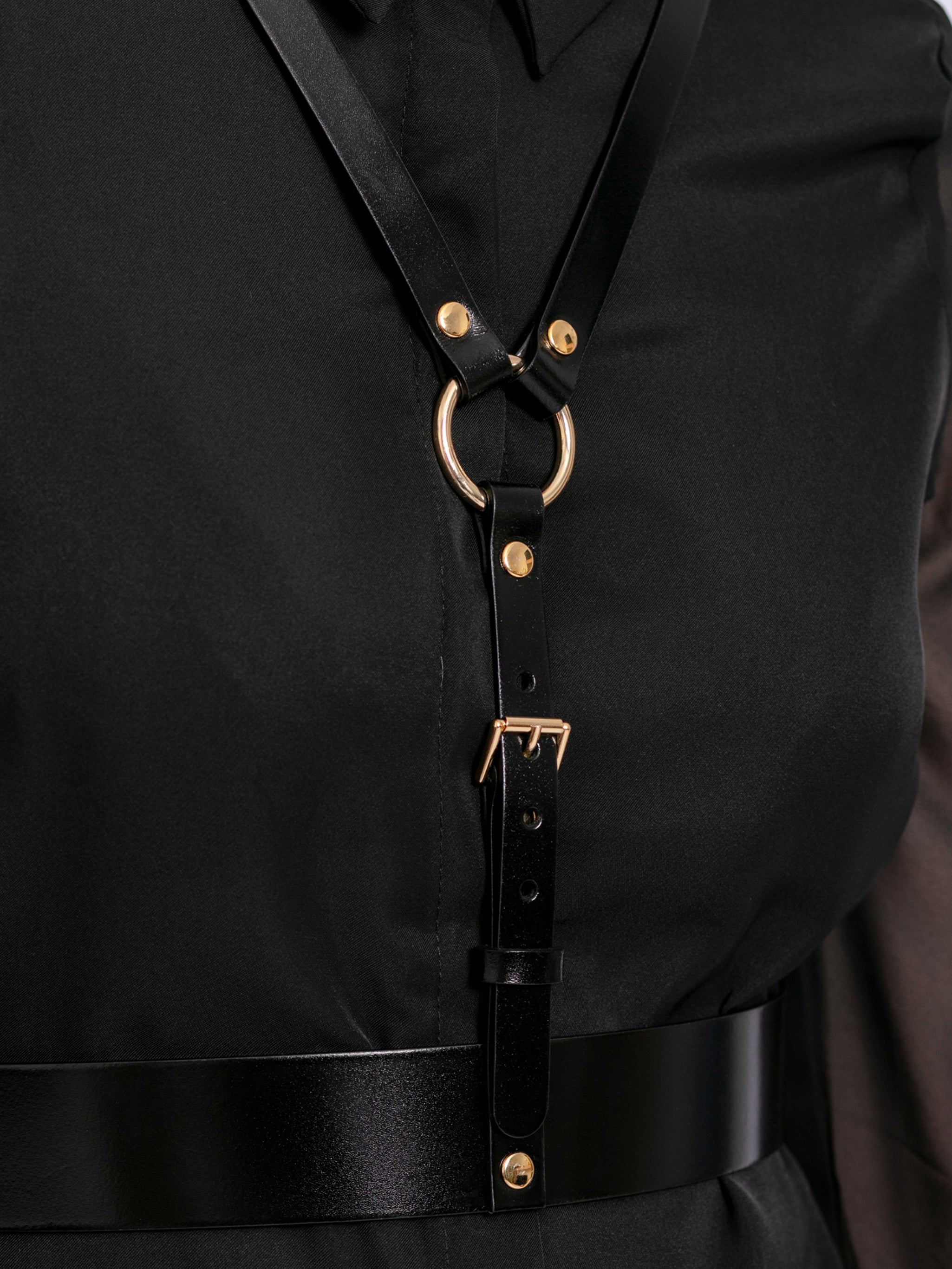 Detailed view of black leather harness worn by model over black shirt.