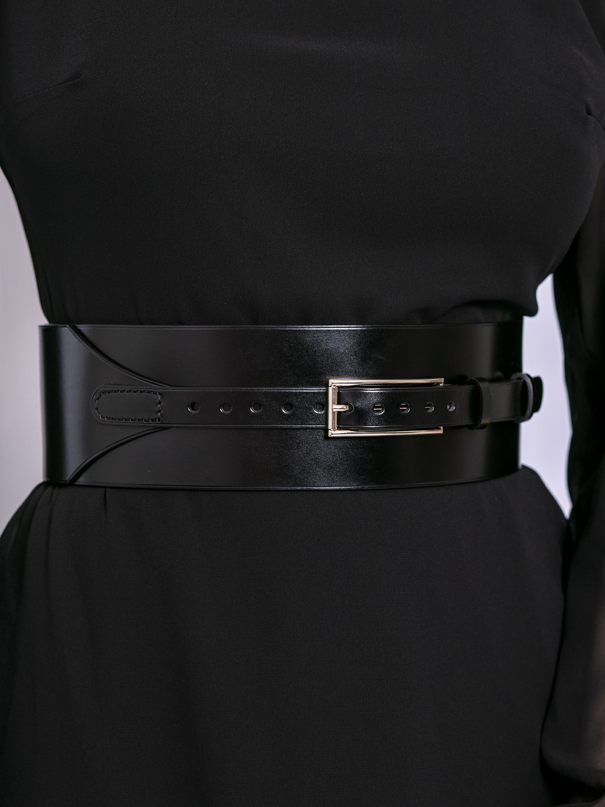 Close view of wide corset belt worn by model over black dress.